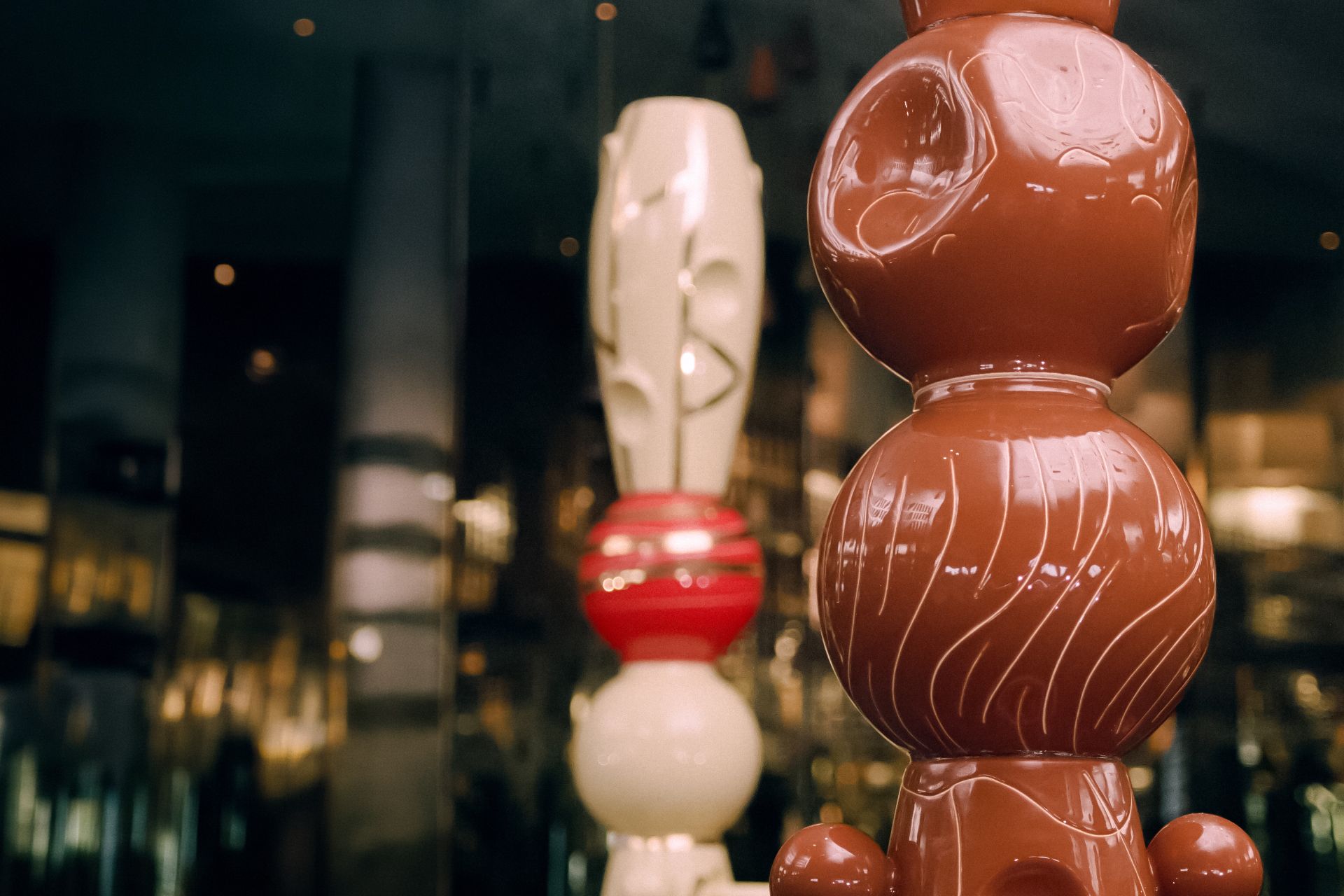 fotografia barwna. Fregment dwóch ceramicznych totemów na rozmazanym tle wnętrza muzeum.
